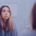 Nachdenkliche Frau vor dem Spiegel. Symbolbild für Grenzen setzen ohne Schuldgefühle, emotionale Überforderung und das Gefühl, beim Abgrenzen herzlos zu sein.