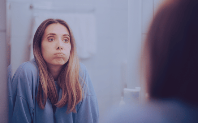 Nachdenkliche Frau vor dem Spiegel. Symbolbild für Grenzen setzen ohne Schuldgefühle, emotionale Überforderung und das Gefühl, beim Abgrenzen herzlos zu sein.